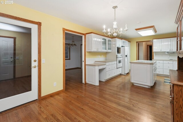 kitchen with white appliances, a chandelier, light wood-style flooring, white cabinetry, and glass insert cabinets