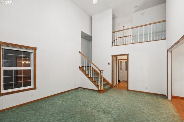 unfurnished living room with a high ceiling, stairway, carpet floors, and baseboards