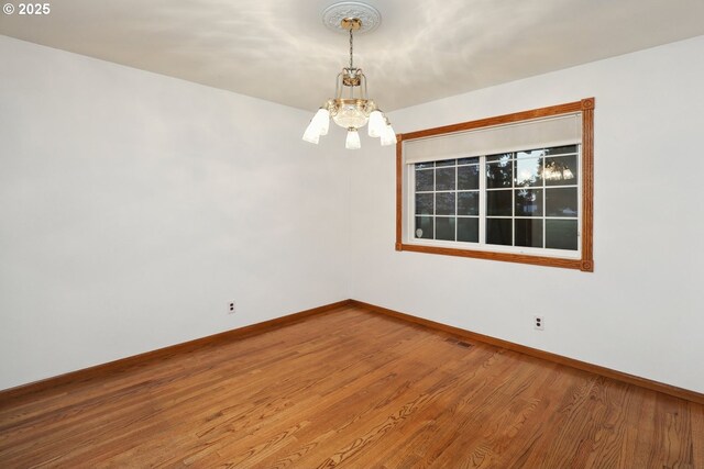 spare room with a chandelier, baseboards, and wood finished floors