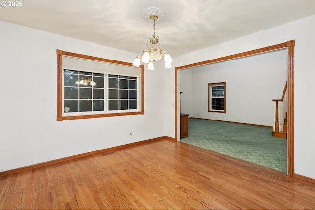 empty room featuring a chandelier, baseboards, and wood finished floors