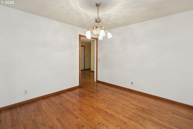 empty room featuring a chandelier, baseboards, and light wood finished floors