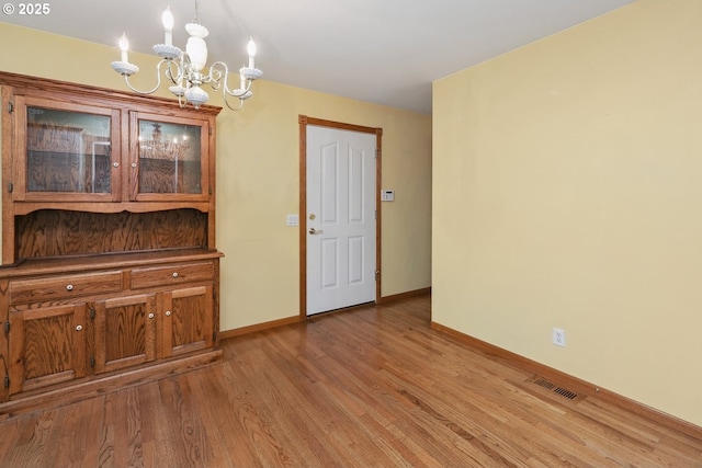 unfurnished dining area with a chandelier, light wood-style flooring, and baseboards