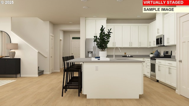 kitchen featuring white cabinetry, light hardwood / wood-style flooring, stainless steel appliances, and a center island with sink