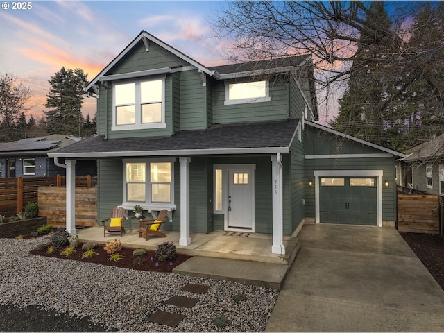 traditional home with fence, concrete driveway, roof with shingles, covered porch, and an attached garage