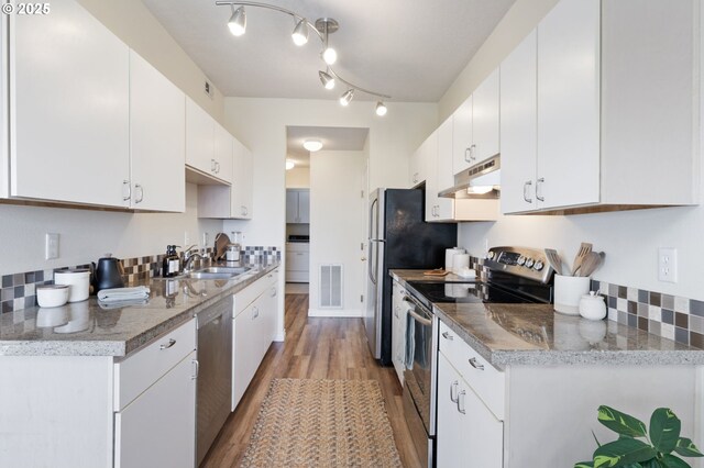 kitchen with stainless steel appliances, a sink, under cabinet range hood, light wood-style flooring, and white cabinets
