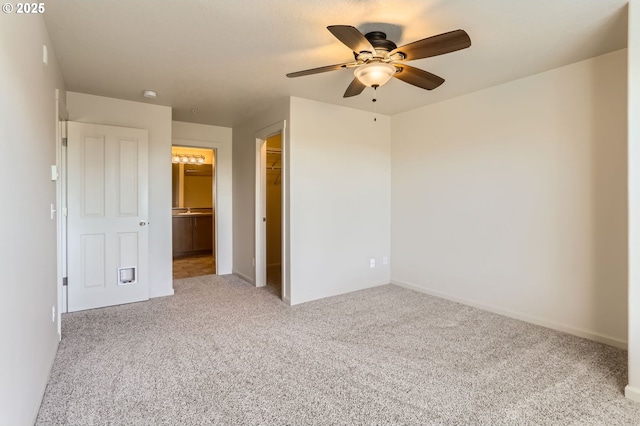 unfurnished bedroom with carpet flooring, a walk in closet, a closet, ensuite bathroom, and a ceiling fan