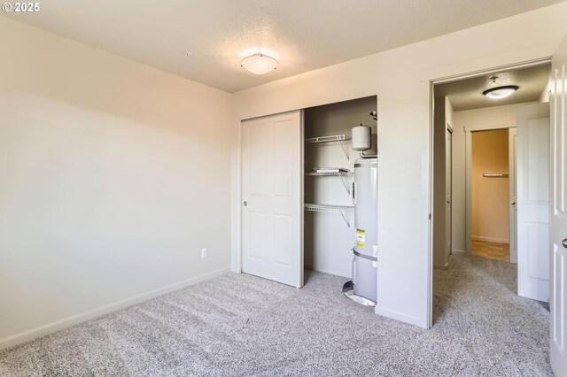 unfurnished bedroom with water heater, carpet flooring, baseboards, and a closet