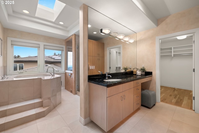 bathroom with tile patterned flooring, vanity, a washtub, and a skylight