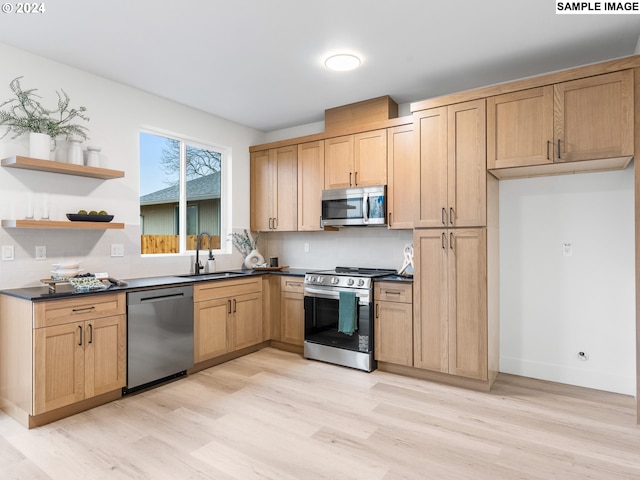 kitchen featuring light brown cabinetry, dark countertops, a sink, light wood-style flooring, and stainless steel appliances
