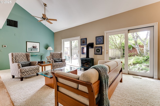 living area with visible vents, a wood stove, a ceiling fan, and high vaulted ceiling