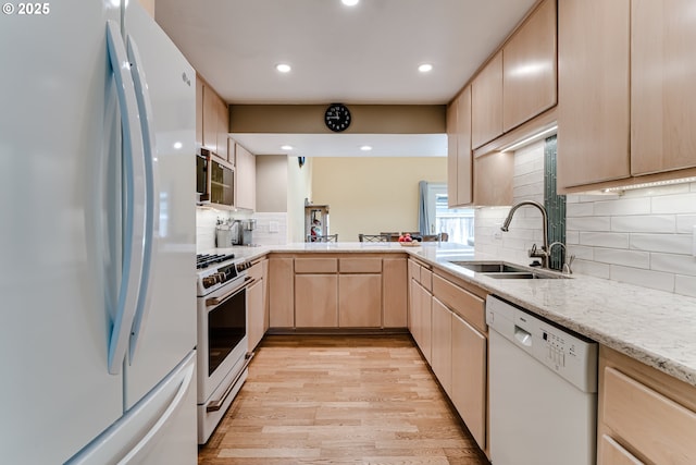 kitchen with light brown cabinetry, tasteful backsplash, a sink, white appliances, and light wood-type flooring