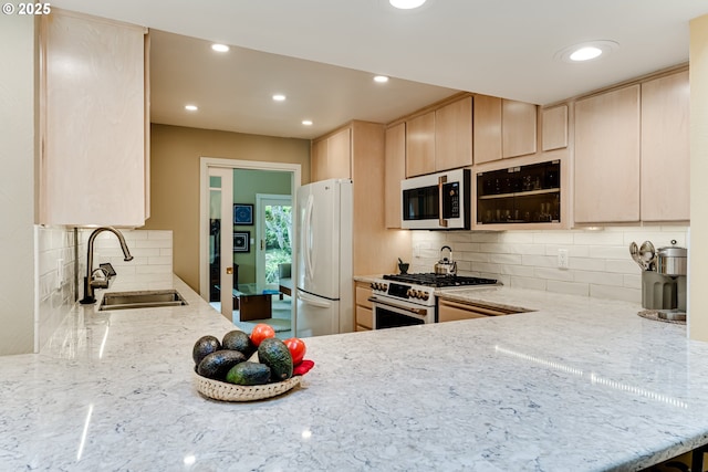 kitchen featuring light brown cabinetry, white appliances, light stone countertops, tasteful backsplash, and a sink