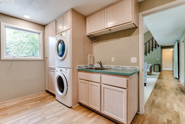 laundry room with cabinet space, stacked washer and dryer, a sink, and light wood-type flooring
