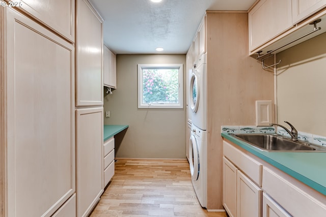 laundry area featuring cabinet space, stacked washer / drying machine, a sink, light wood finished floors, and recessed lighting