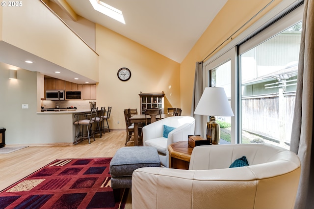 living area with a skylight, high vaulted ceiling, wood finished floors, and a wealth of natural light