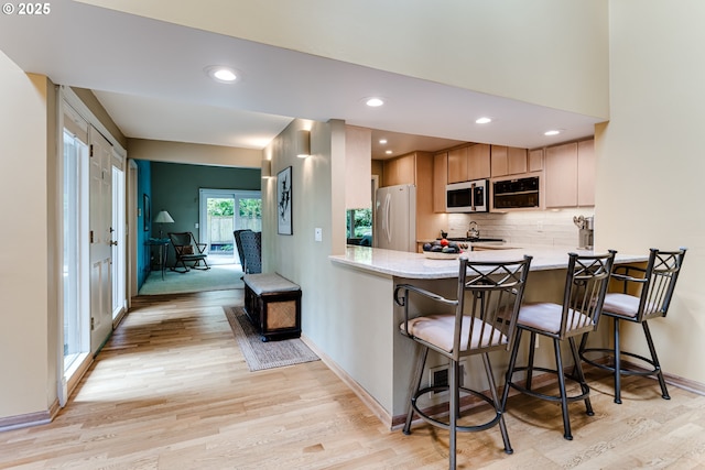 kitchen featuring decorative backsplash, freestanding refrigerator, a peninsula, and light wood-style flooring