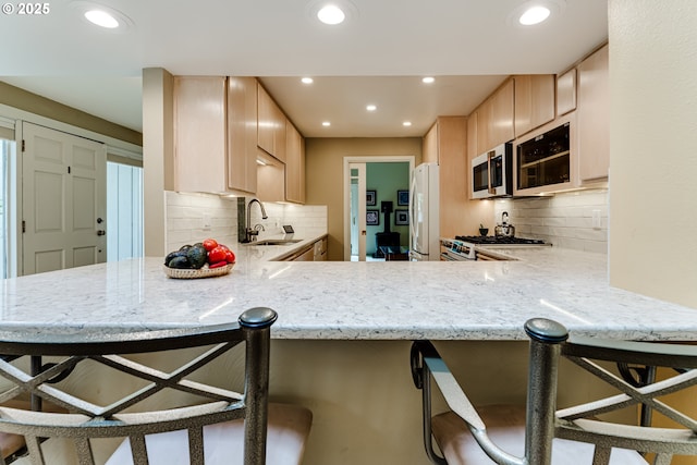 kitchen with a sink, light brown cabinets, freestanding refrigerator, stainless steel microwave, and tasteful backsplash