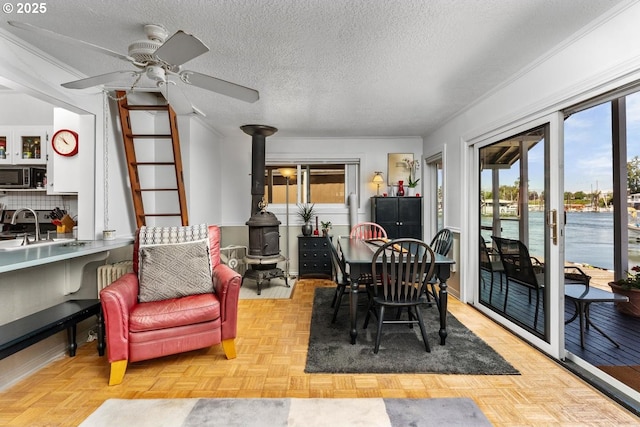 dining room featuring a wood stove, a water view, ceiling fan, a textured ceiling, and light parquet flooring