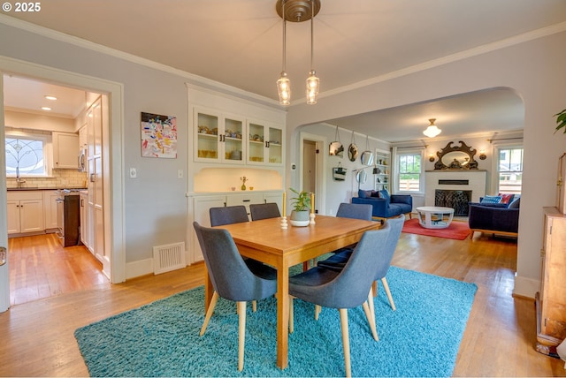 dining room featuring arched walkways, light wood-style flooring, a fireplace, ornamental molding, and baseboards