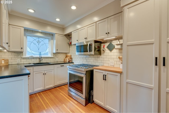 kitchen with appliances with stainless steel finishes, a sink, light wood-type flooring, crown molding, and white cabinets
