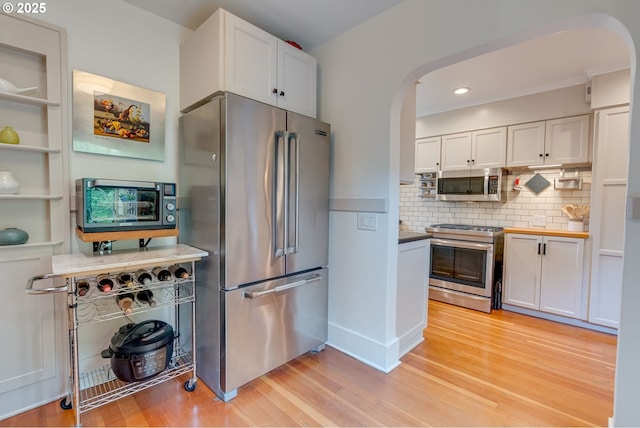 kitchen featuring appliances with stainless steel finishes, arched walkways, light wood-type flooring, white cabinets, and recessed lighting