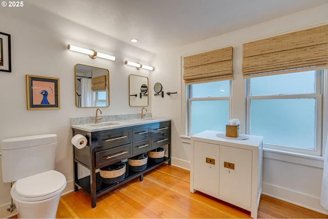 full bathroom featuring wood finished floors, toilet, double vanity, and baseboards