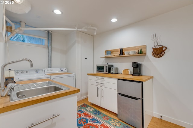 kitchen featuring freestanding refrigerator, wooden counters, a sink, independent washer and dryer, and white cabinetry