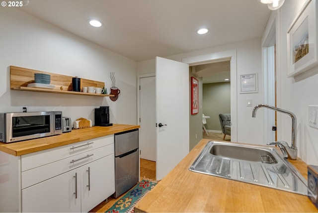 kitchen with wood counters, refrigerator, a sink, white cabinetry, and stainless steel microwave