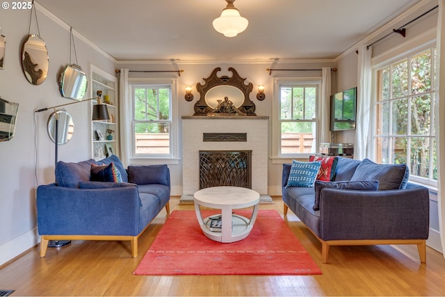 living room featuring wood finished floors, healthy amount of natural light, a brick fireplace, crown molding, and baseboards