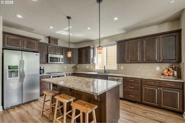 10380 SW Madrid Loop, Wilsonville, OR 97070 - kitchen featuring appliances with stainless steel finishes, dark brown cabinetry, light wood finished floors, a kitchen bar, and recessed lighting