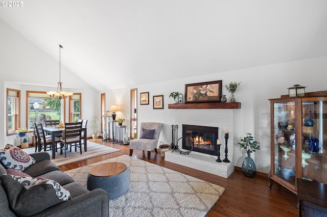 living area with baseboards, a chandelier, wood finished floors, a brick fireplace, and high vaulted ceiling