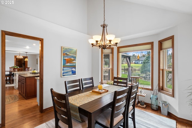 dining space featuring baseboards, high vaulted ceiling, an inviting chandelier, and light wood-style floors