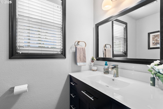 bathroom with a textured wall, visible vents, and vanity