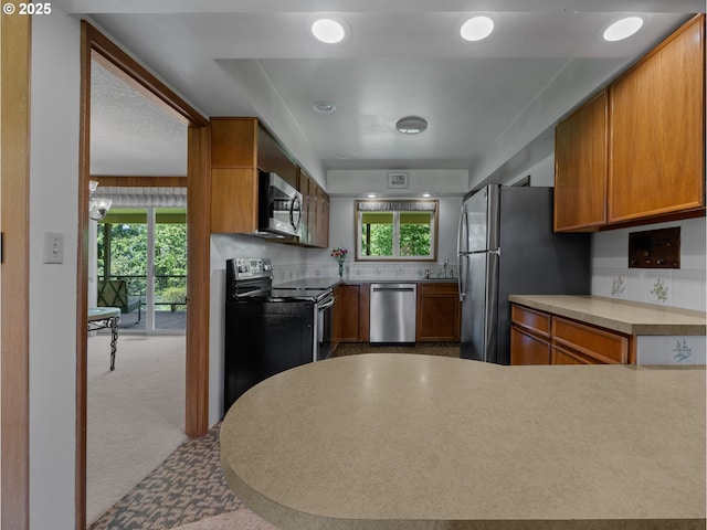 kitchen with brown cabinets, appliances with stainless steel finishes, a sink, light countertops, and a peninsula