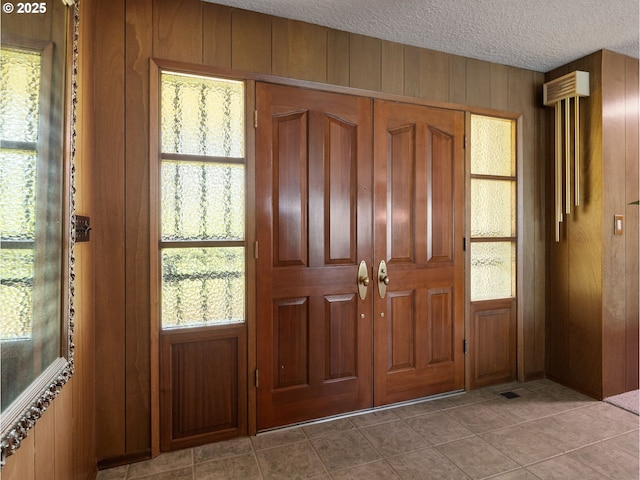 foyer entrance with wooden walls, a textured ceiling, a wealth of natural light, and light tile patterned floors
