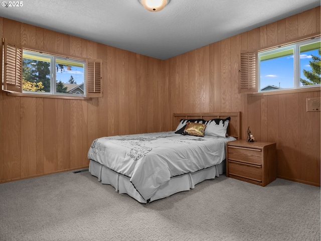 bedroom with wooden walls, a textured ceiling, and light carpet
