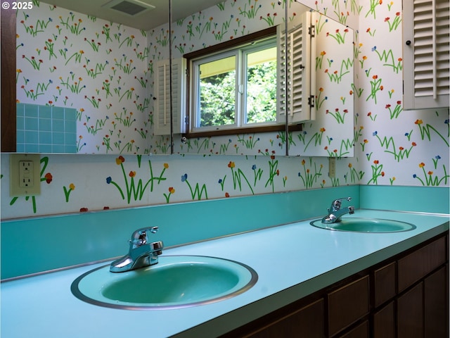 full bath with a sink, wallpapered walls, double vanity, and visible vents