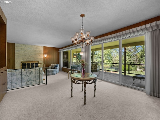 dining space with a notable chandelier, a brick fireplace, a textured ceiling, wood walls, and carpet
