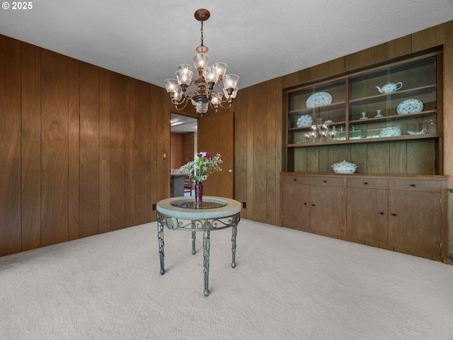 carpeted dining room featuring wooden walls, built in features, and a chandelier