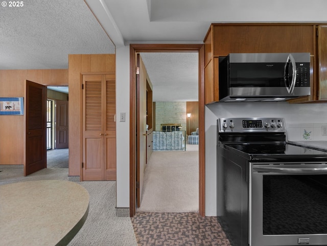 kitchen featuring wood walls, a textured ceiling, appliances with stainless steel finishes, and light carpet