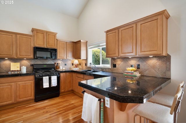 kitchen with black appliances, a sink, a breakfast bar, light wood finished floors, and high vaulted ceiling