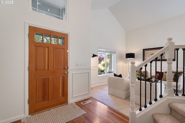 entryway featuring high vaulted ceiling, wood finished floors, stairs, wainscoting, and a decorative wall