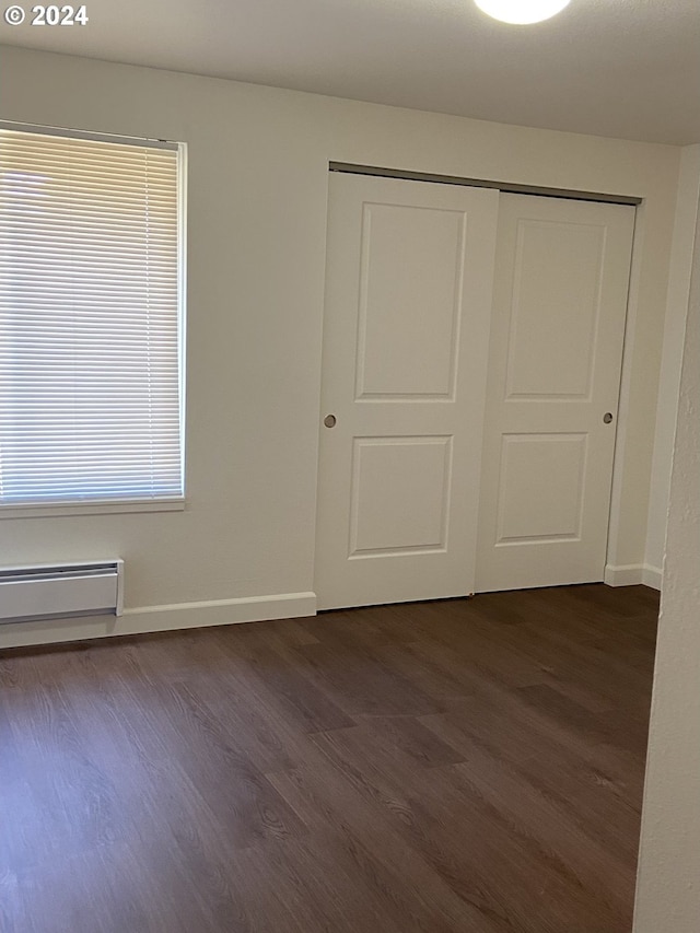 unfurnished bedroom with dark wood-type flooring, a closet, and baseboard heating