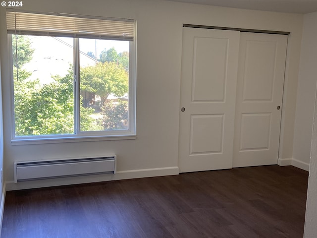 unfurnished bedroom featuring multiple windows, dark wood-type flooring, baseboard heating, and a closet