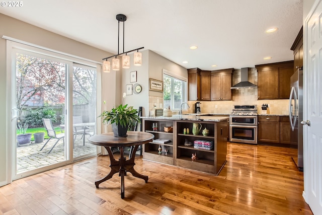 kitchen featuring tasteful backsplash, wall chimney range hood, plenty of natural light, light wood-style flooring, and stainless steel appliances