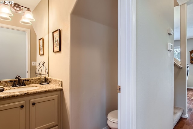 half bathroom with toilet, wood finished floors, vanity, and baseboards