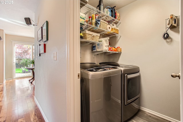 washroom with laundry area, wood finished floors, washing machine and clothes dryer, and baseboards