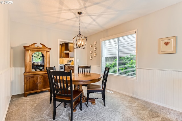 dining space with light colored carpet, wainscoting, and an inviting chandelier