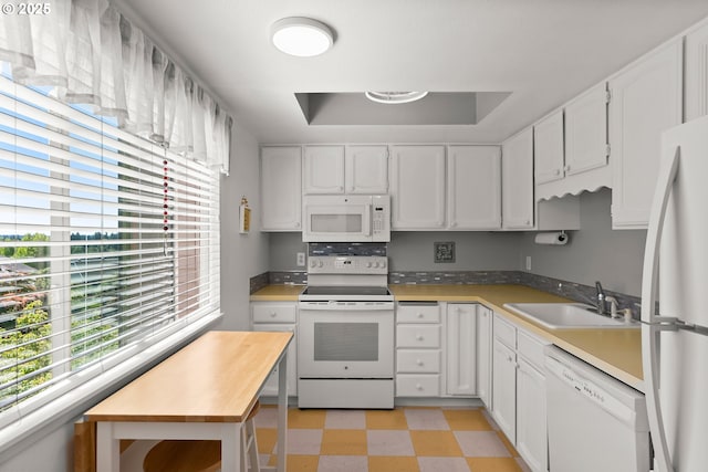 kitchen featuring white appliances, a sink, light floors, and white cabinetry