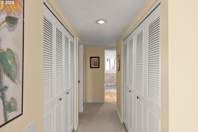 corridor with light colored carpet, a textured ceiling, and baseboards